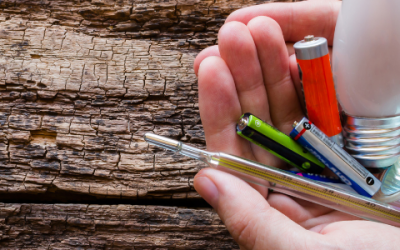 Universal waste of batteries, bulbs and thermometers held in hand with wood background